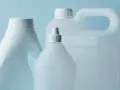 Trzy białe plastikowe butelki z uchwytami i nakrętkami na jasnoniebieskim tle.