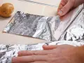 Ręce rozwijają folię aluminiową obok ziemniaków. Zastanawiasz się, gdzie wyrzucić folię aluminiową?