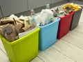 Cztery kolorowe kosze na śmieci z posegregowanymi odpadami: papier, plastik, metal i bio.