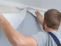 Mężczyzna zdejmuje starą tapetę ze ściany za pomocą narzędzia.