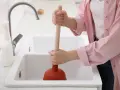 Osoba używa przepychacza, by udrożnić rurę do szamba.