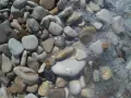 Gładkie, zaokrąglone kamienie, idealne jako kamień pod drenaż oczyszczalni. Woda z pianą obmywa brzeg.