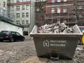 Kontener na śmieci z napisem "Przyjazny Recykling" wypełniony papierem. W tle budynki i czarny samochód. Data: 17 09 04.
