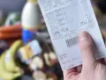 Ręka trzyma paragon z zakupów spożywczych, na którym widnieje suma 250,02 zł. Zastanawiasz się, gdzie wyrzucać paragony? Ten jest z papieru termicznego.