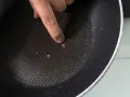 Palec wskazujący na uszkodzoną powłokę patelni. Czas na recykling i pytanie: gdzie wyrzucić patelnię?