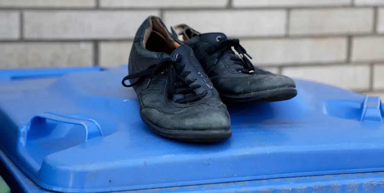 Stare, czarne buty leżą na niebieskim koszu na śmieci. Czas zastanowić się, gdzie wyrzucić stare buty, by dać im drugie życie.