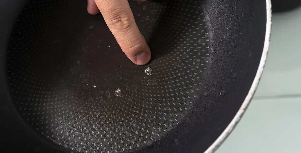 Palec wskazujący na uszkodzoną powłokę patelni. Czas na recykling i pytanie: gdzie wyrzucić patelnię?