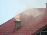 Dym z komina, unoszący się nad czerwonym dachem, niesie ze sobą zapach palonego drewna i trochę sadzy.