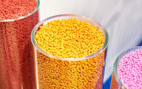 Trzy przezroczyste cylindry wypełnione kolorowymi granulkami plastiku: czerwonym, żółtym i różowym.