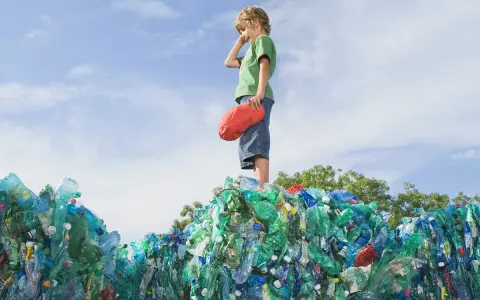 Chłopiec stoi na górze sterty plastikowych butelek, zastanawiając się, co to za pla.