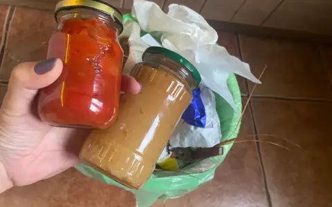 Dwie słoiki z przetworami, jeden z papryką, drugi z dżemem, trafiają do kosza. Tak wygląda prawidłowe wyrzucanie starych przetworów.