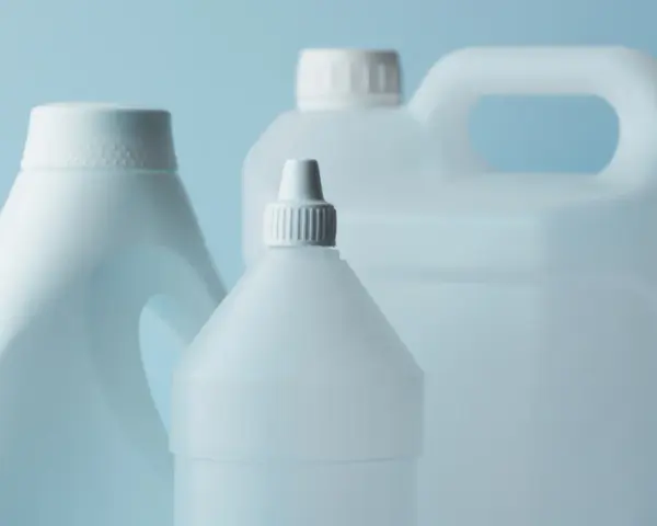 Trzy białe plastikowe butelki z uchwytami i nakrętkami na jasnoniebieskim tle.