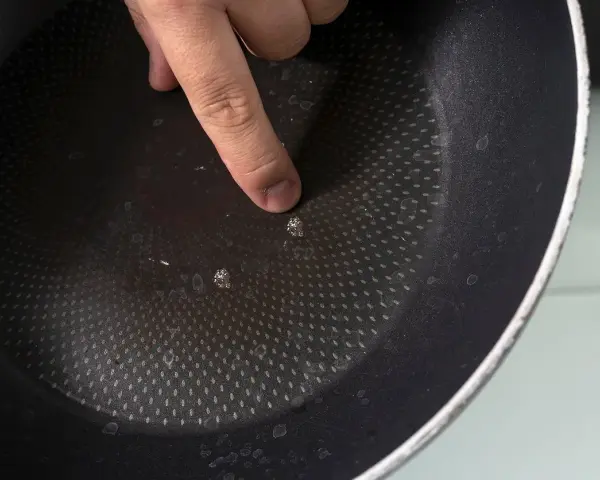 Palec wskazujący na uszkodzoną powłokę patelni. Czas na recykling i pytanie: gdzie wyrzucić patelnię?