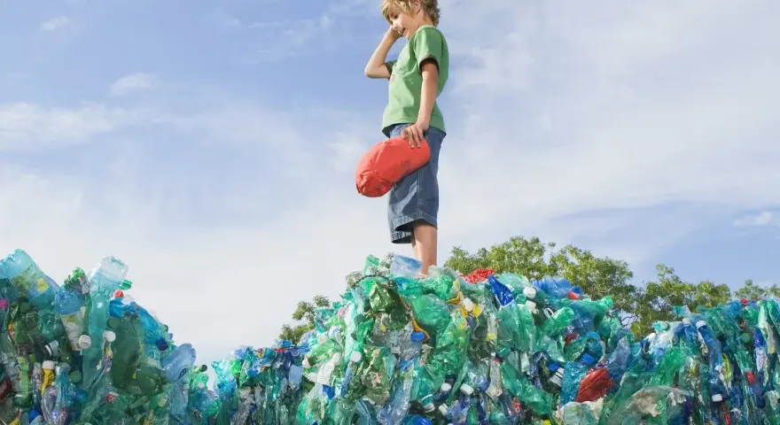 Chłopiec stoi na górze sterty plastikowych butelek, zastanawiając się, co to za pla.