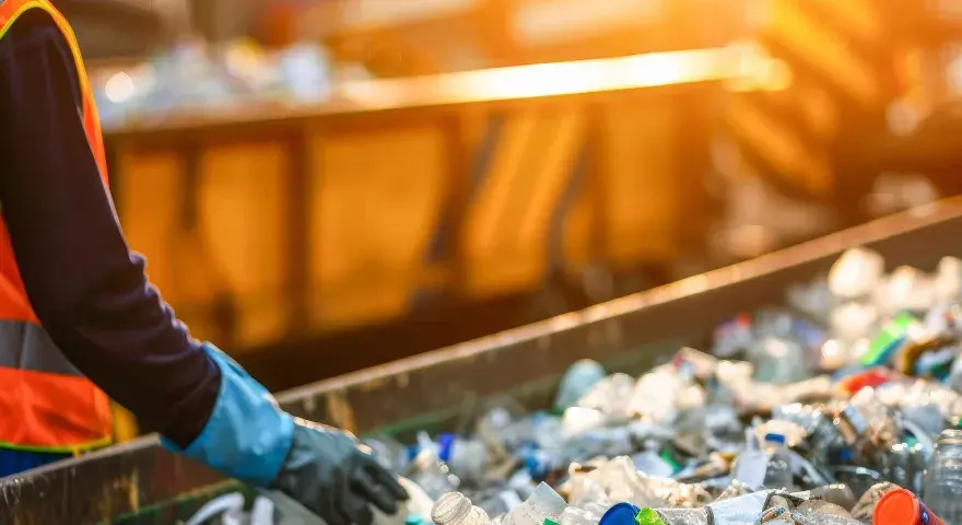 Pracownik w kamizelce odblaskowej sortuje plastikowe butelki na taśmie. Data 191204.