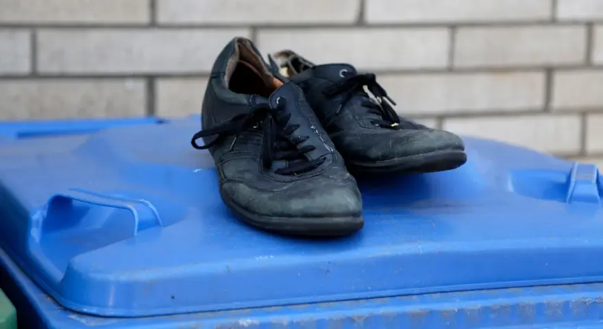 Stare, czarne buty leżą na niebieskim koszu na śmieci. Czas zastanowić się, gdzie wyrzucić stare buty, by dać im drugie życie.