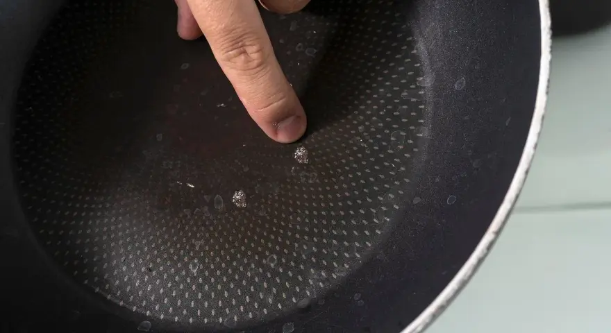 Palec wskazujący na uszkodzoną powłokę patelni. Czas na recykling i pytanie: gdzie wyrzucić patelnię?