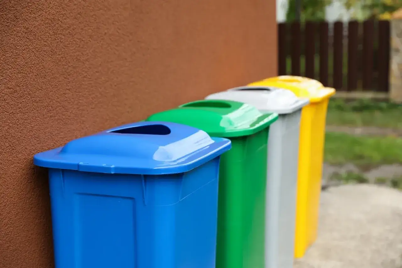 Kolorowe kosze na śmieci, gdzie wyrzucać kapsułki po kawie. Niebieski, zielony, szary i żółty stoją obok siebie.