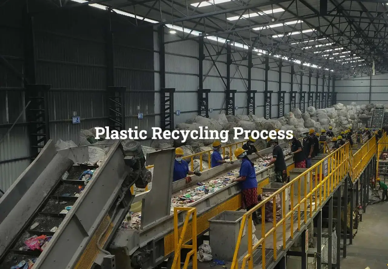 Pracownicy sortują odpady plastikowe na taśmie w hali recyklingu. W tle widać sterty worków z przetworzonym materiałem, np. rPET.