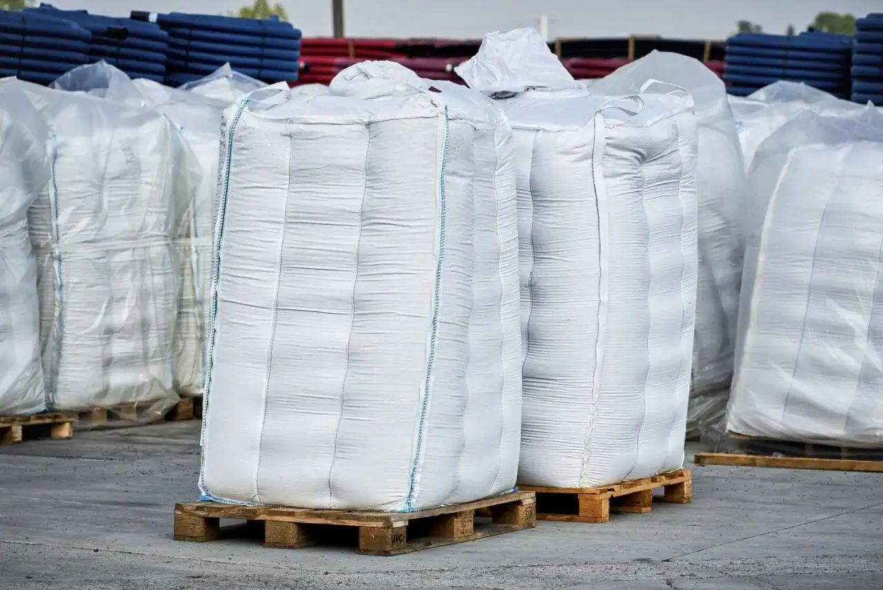 Duże, białe worki z tworzywa sztucznego, wypełnione granulatem HDPE, stoją na drewnianych paletach.